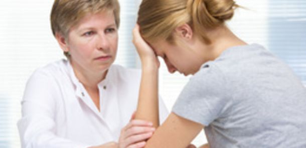 Eine Ärztin sitzt mit einer Patientin am Tisch, die ihr Gesicht verzweifelt auf eine Hand stützt